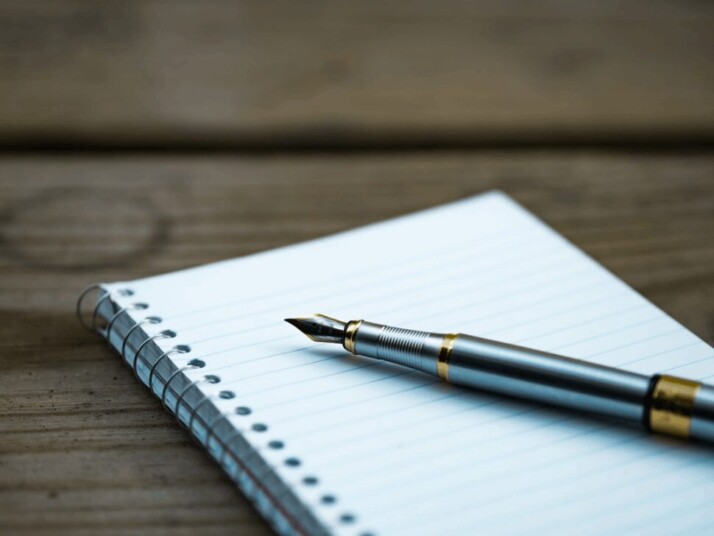 Fountain pen and white spiral book on brown table