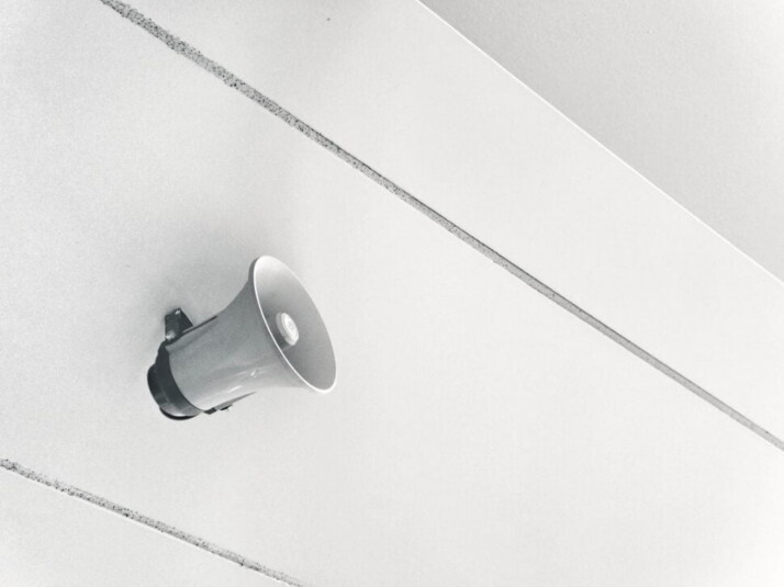 A gray megaphone that is hanging on a white wall