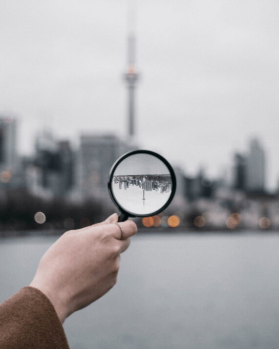 A person holding magnifying glass directed at a city.