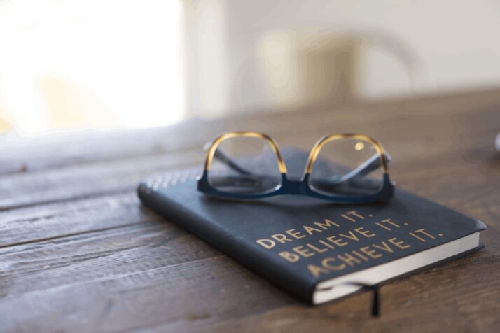black and brown eyeglasses on a book on brown wooden table