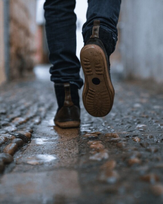 close-up photography of person walking on wet cobblestone pavement.