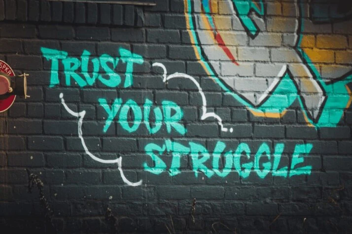 green trust your struggle graffiti on black background with painting beside it