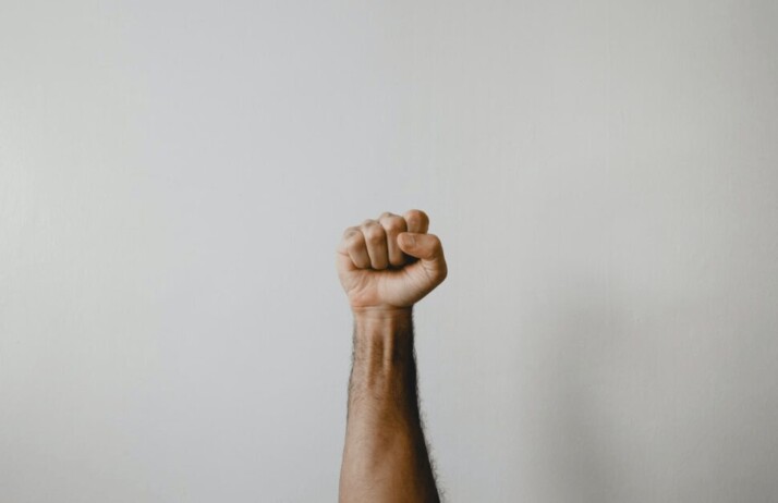 persons right hand clenched as a fist before a white wall