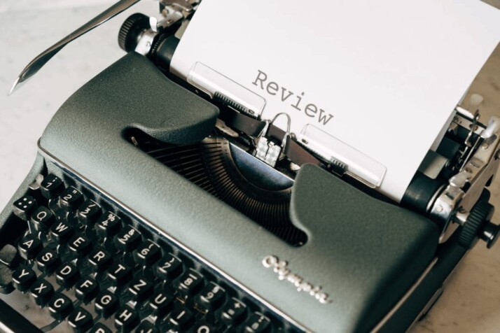 a dark green typewriter on white table with a paper that says review.