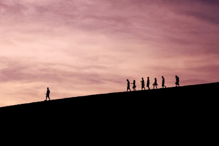 silhouette of people on hill and their leader in front of them.