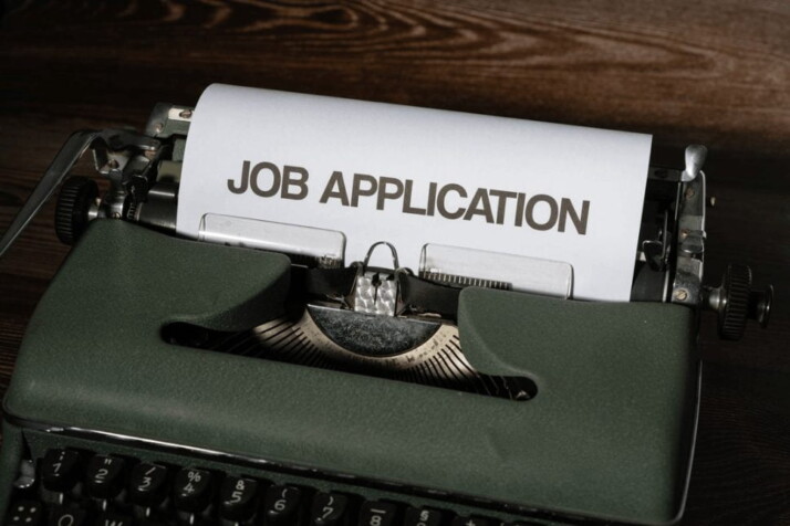 a green typewriter printing out a page that reads job application in bold lettering.