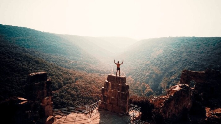 A person standing on a brown concrete building overlooking a valley of trees