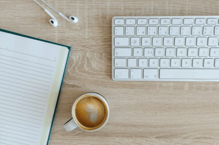 coffee latte near white wireless keyboard and Apple EarPods on the table photography