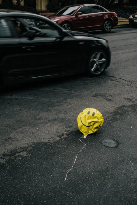 smiling disinflated emoji balloon beside black BMW 3 series during daytime