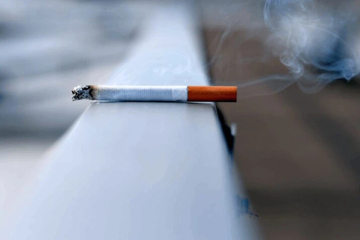 A white lit cigarette stick kept on a white wall.