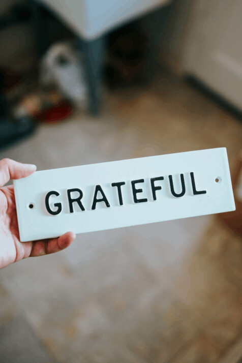 person holding white and black plate that reads grateful.