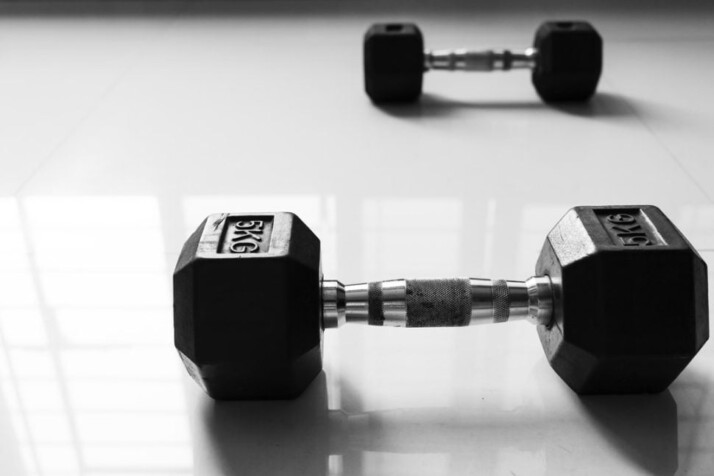 Two black dumbbells are placed on a white tiled floor. 