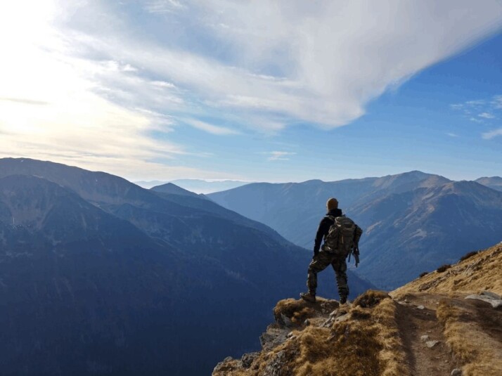 A man on top of mountain under blue sky.