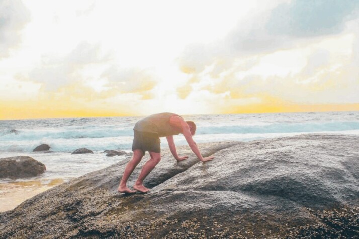 A man leaning on gray rock near a body of water