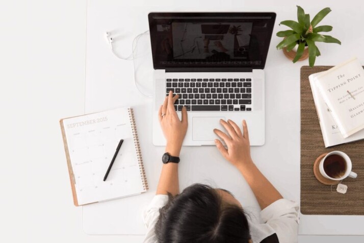 A person working on a MacBook Pro with tea and notepad on either sides. 