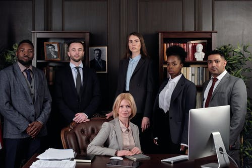 people posing behind lady wearing silver jacket and sitting on brown chair