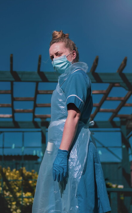 Nurse standing while wearing a hand glove and nose mask