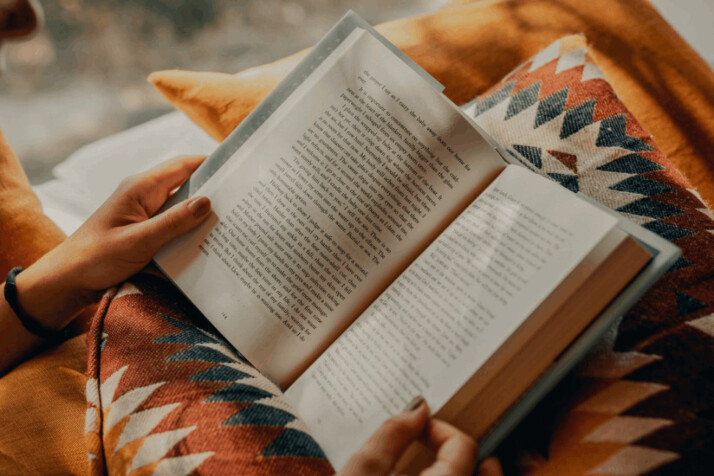 person reading book on brown and beige pillow with textile design