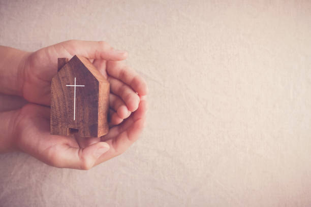 child hands holding wooden carved church in open palms. 