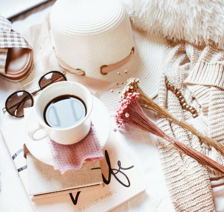 A cup of coffee surrounded by glasses, a hat, and flowers.