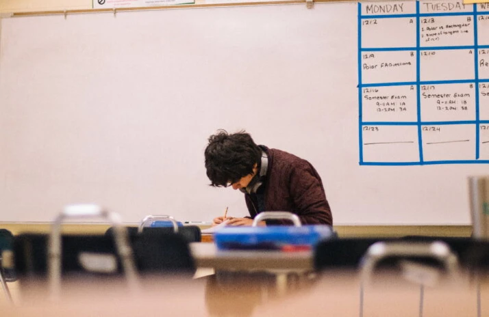 A student writing down something while sitting in a classroom.