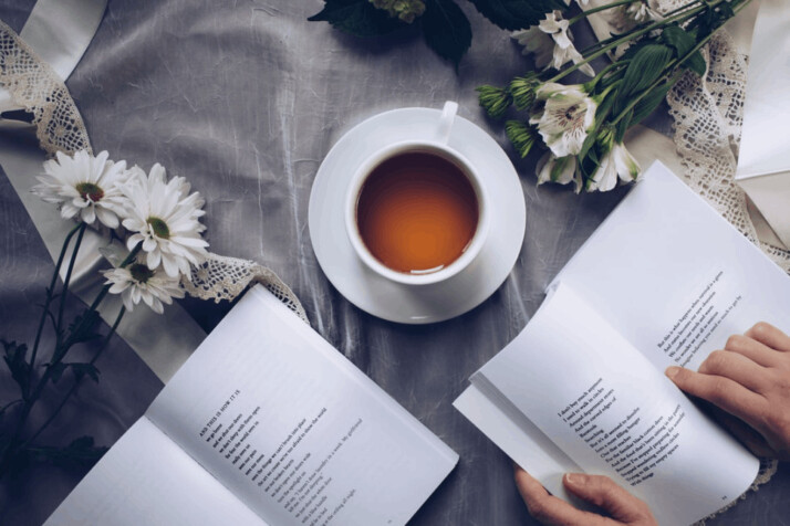 A white cup with saucer near a book and flower sticks surrounding it. 