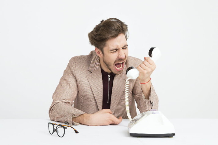A man screaming into a telephone looking angry and frustrated.