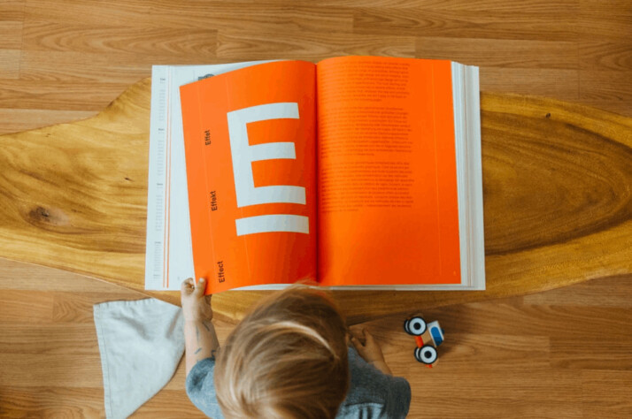 A little kid reading a book with a big letter E on one page.