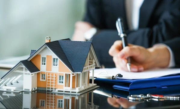 person writing on paper near house model on a glass table 