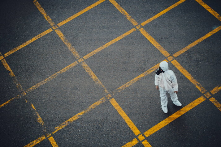 A person wearing a HAZMAT suit and a gas mask standing over a yellow grid.
