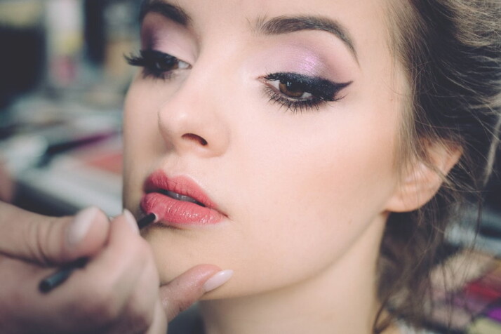 A pretty woman getting her lips applied with lipstick.