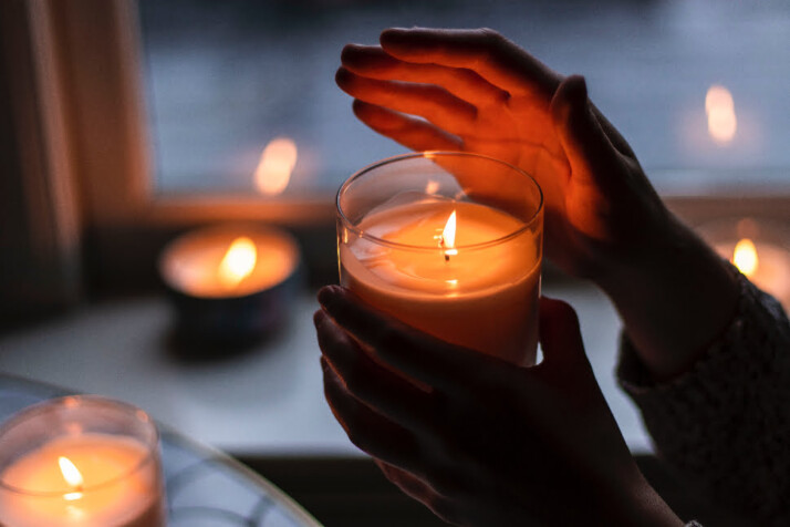 A person holding a scented candle that's already lit.