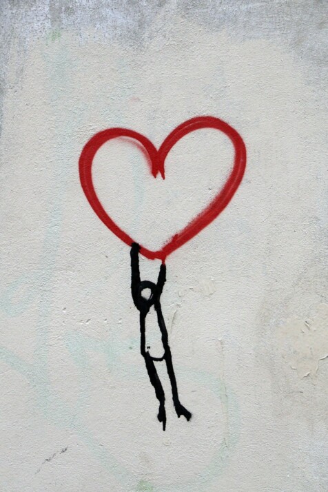 A wall painting of a red heart carried by a stick figure