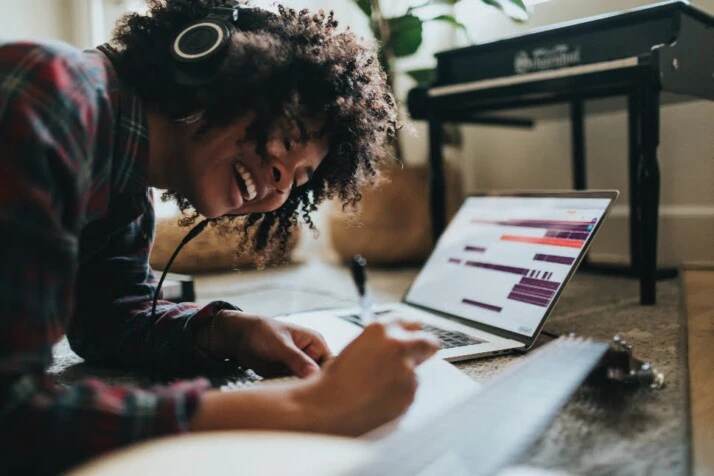 a young black woman writing songs while listening to music.