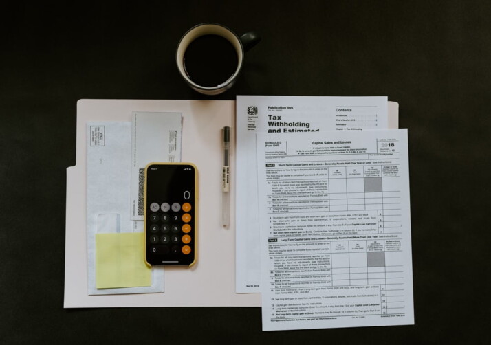 A collection of things you need for tax filing: Phone, pen, folder, tax papers.
