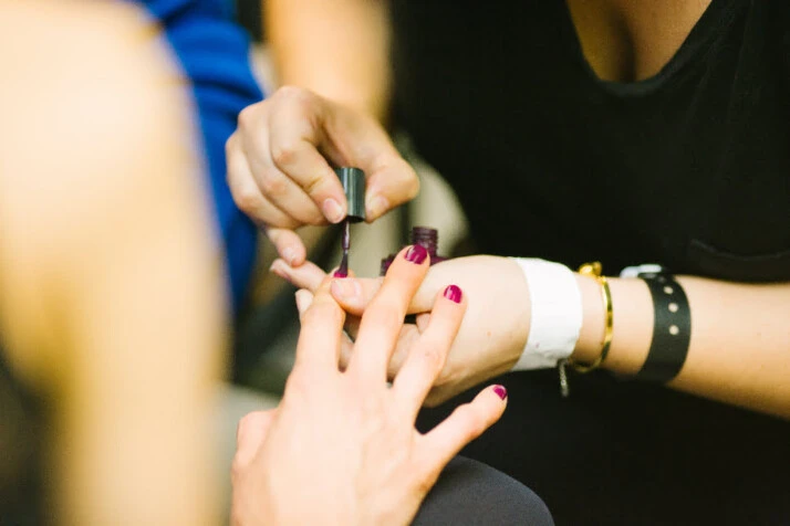 A woman painting the nail of the index finger of another woman.