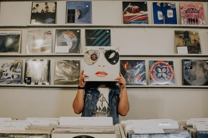 A person covering face with hipster vinyl sleeve and hipster art in the background 