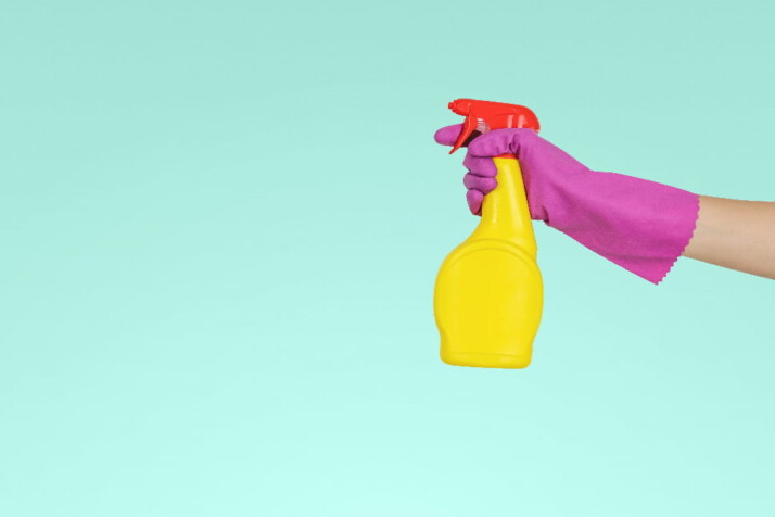 A hand wearing a pink glove holding a yellow spray.