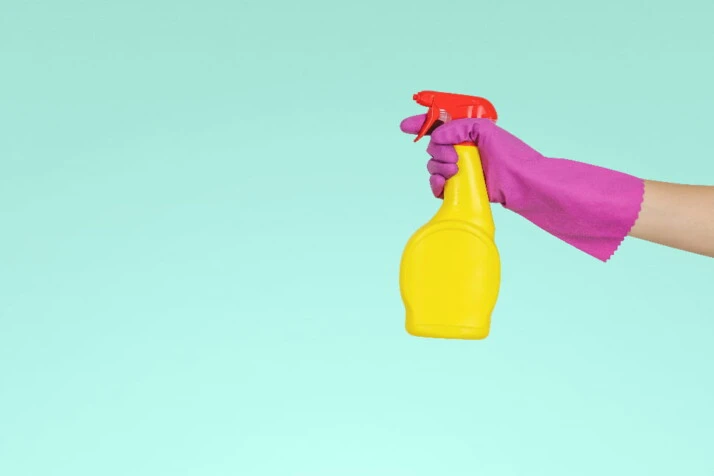 A hand wearing a pink glove holding a yellow spray.