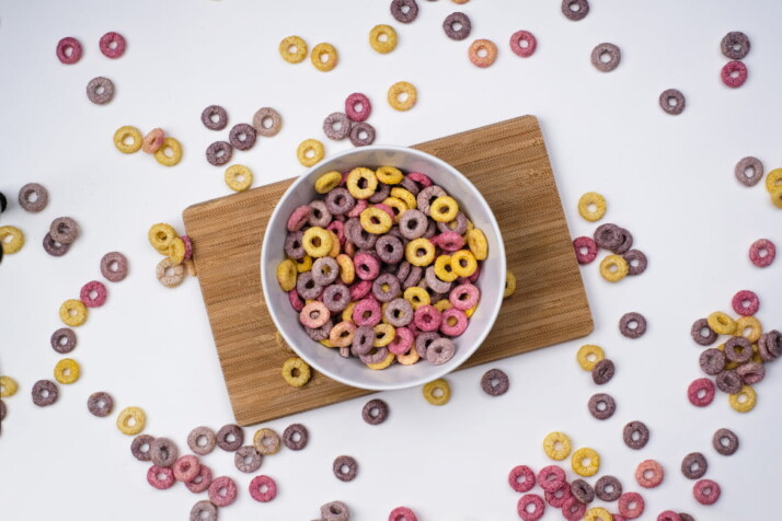 A bowl of cereal with scattered cereal bits surrounding it.