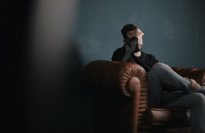 A man wearing sitting on a couch with his head held in one hand