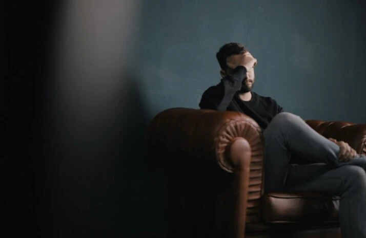 A man wearing sitting on a couch with his head held in one hand