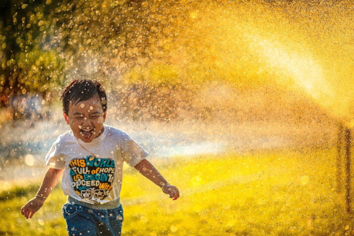 A little boy laughing and running as the water splashes on him