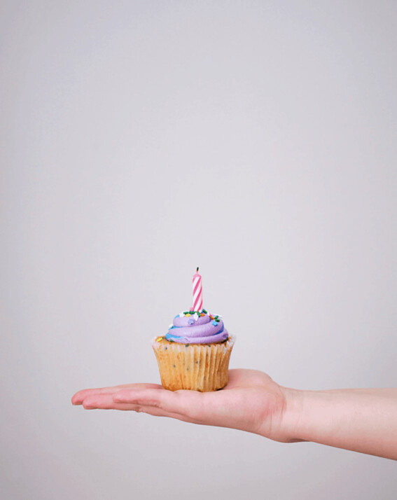 cupcake with candle atop a hand with a blank, white wall background