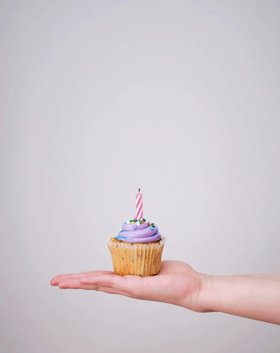 cupcake with candle atop a hand with a blank, white wall background