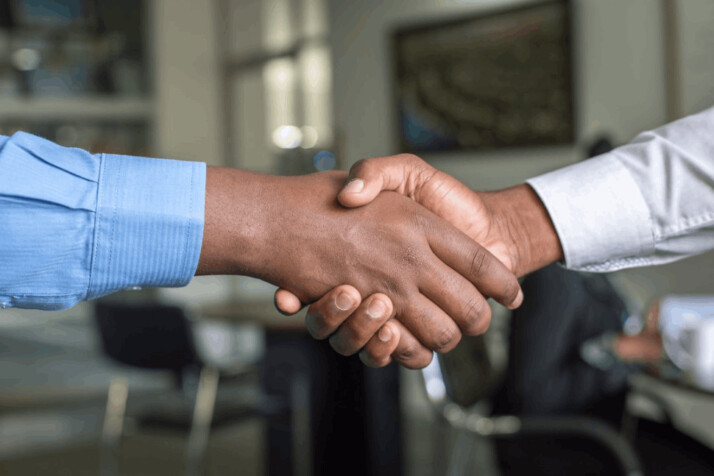 two people shaking hands with a man wearing blue sleeves and another wearing white