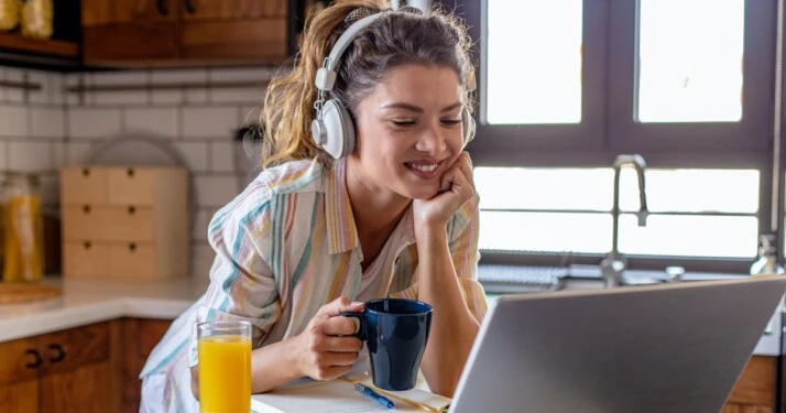 woman with earphones on holding cup and staring at the laptop