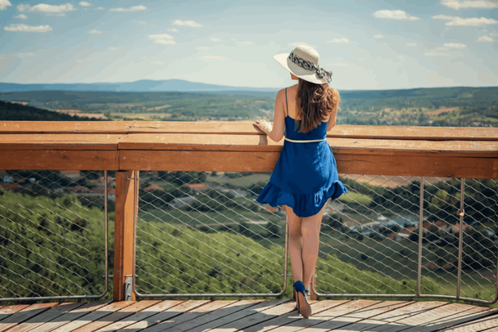 woman in blue sleeveless dress wearing white hat standing on brown wooden bridge during daytime