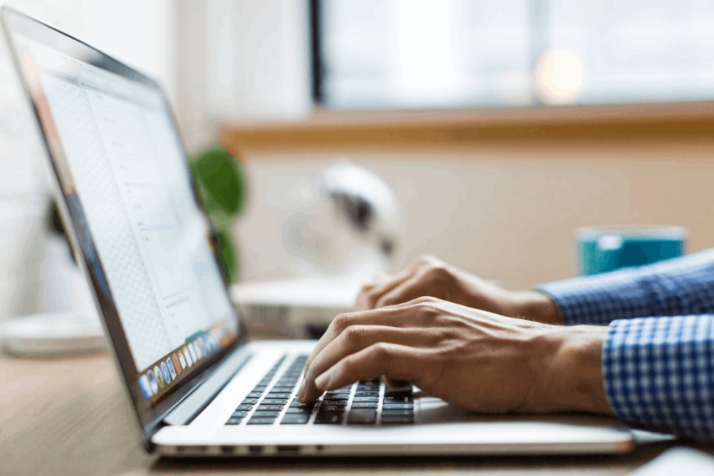 person wearing long sleeve blue shirt typing on silver MacBook