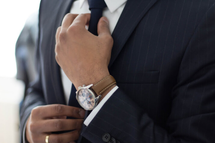 A man wearing a nice watch, fixing his tie.